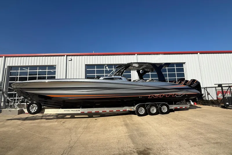 Slide: The Image of 2017 MTI 42V boat on trailer, parked outside a garage under clear blue sky. - 5