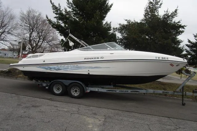 The Image of 2009 Rinker 276 Captiva Bowrider on trailer, parked on street, surrounded by trees. - 1