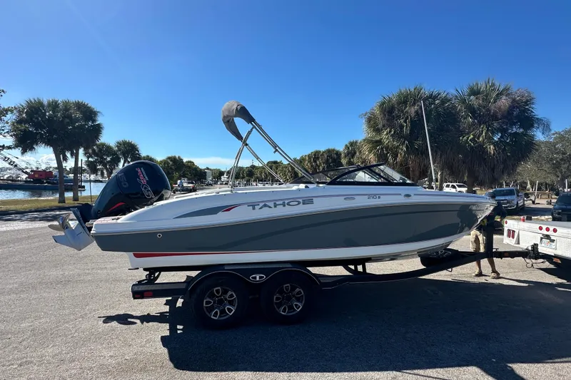 Slide: The Image of 2021 Tahoe 210 S boat on trailer, parked near palm trees under clear blue sky. - 6