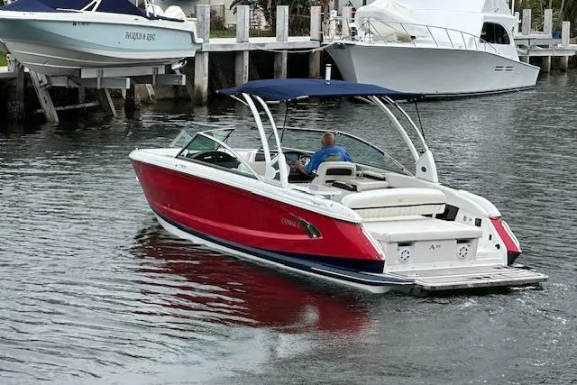Slide: The Image of 2016 Cobalt A28 boat with red hull and blue canopy cruising in marina. - 24