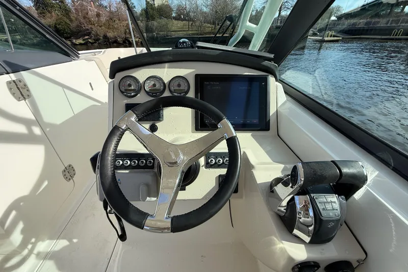 Slide: The Image of 2014 Boston Whaler 270 Vantage helm with steering wheel and control panel by the water. - 17