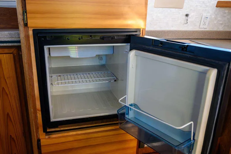 Slide: The Image of Open refrigerator inside 1997 Mainship 350 Trawler, showcasing wooden cabinetry and interior shelving. - 37