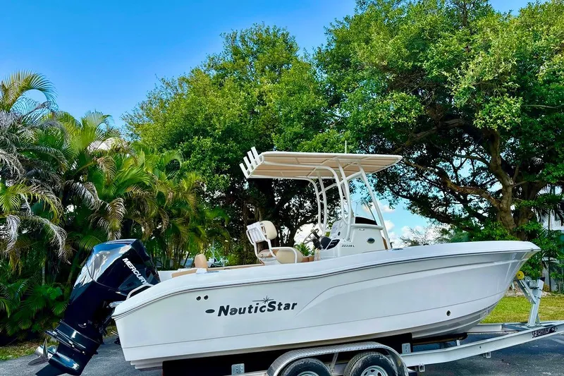 Slide: The Image of 2024 NauticStar 222 Offshore boat on trailer, surrounded by lush greenery. - 2