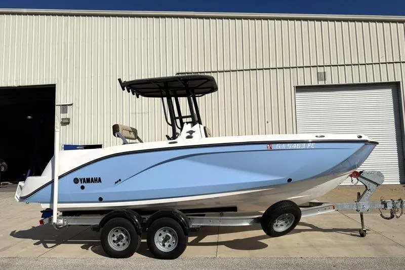 The Image of 2024 Yamaha Boats 222 FSH Sport on trailer, parked outside a warehouse. - 0