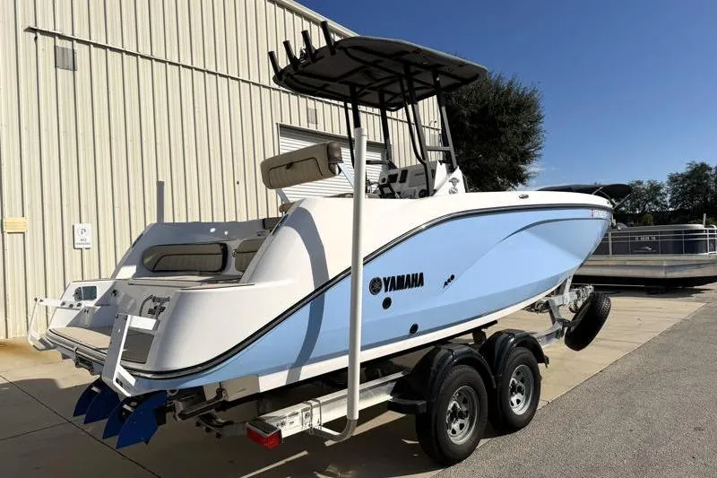 Slide: The Image of 2024 Yamaha Boats 222 FSH Sport on trailer, blue and white design, parked outdoors. - 2