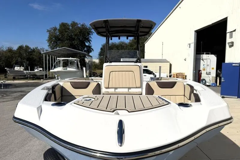 Slide: The Image of 2024 Yamaha Boats 222 FSH Sport, white exterior, docked near a warehouse under clear blue sky. - 6