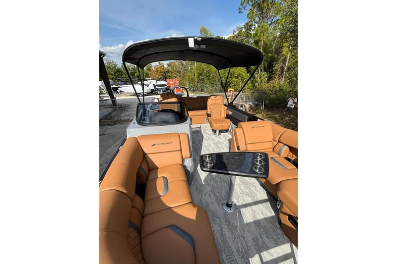 Slide: The Image of 2026 Starcraft RX 23 Q DH boat interior with tan seating and canopy, surrounded by trees. - 13