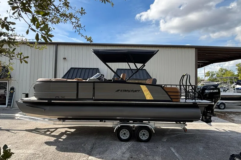Slide: The Image of 2026 Starcraft RX 23 Q DH pontoon boat on trailer, parked outside a warehouse. - 4