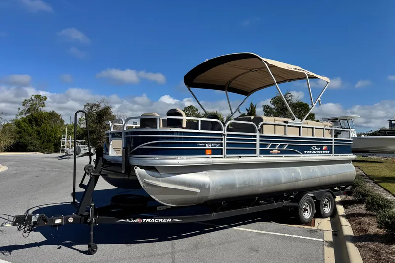 The Image of 2023 Sun Tracker Fishin' Barge 20 DLX pontoon boat on trailer, parked outdoors. - 1