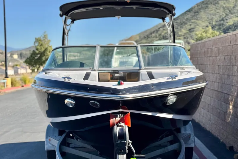 Slide: The Image of 2019 Regal 2100 boat on trailer, parked outdoors with scenic mountain backdrop. - 2