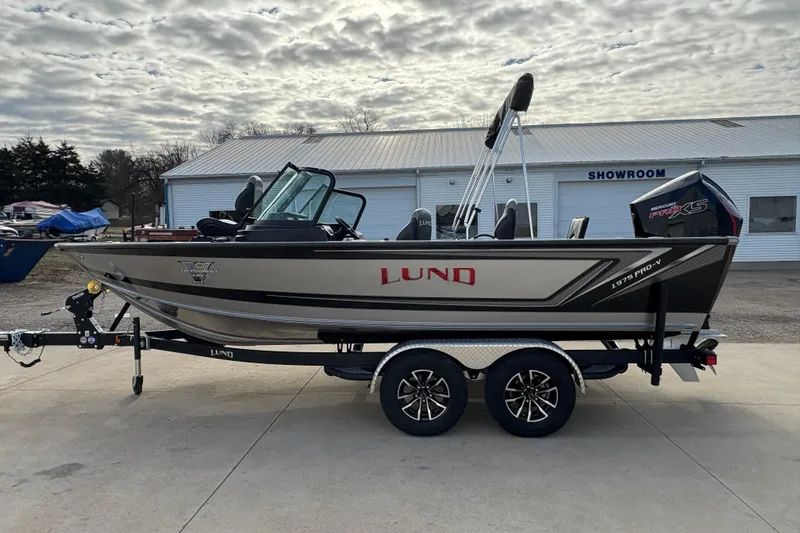 Slide: The Image of 2026 Lund 1975 Pro-V Sport boat on trailer, parked outside a showroom under cloudy sky. - 5