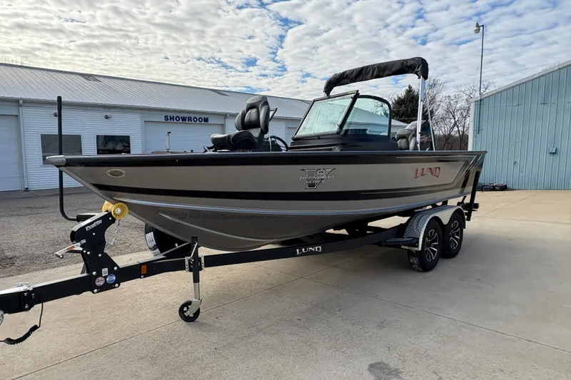 Slide: The Image of 2026 Lund 1975 Pro-V Sport boat on trailer outside showroom, under cloudy sky. - 6