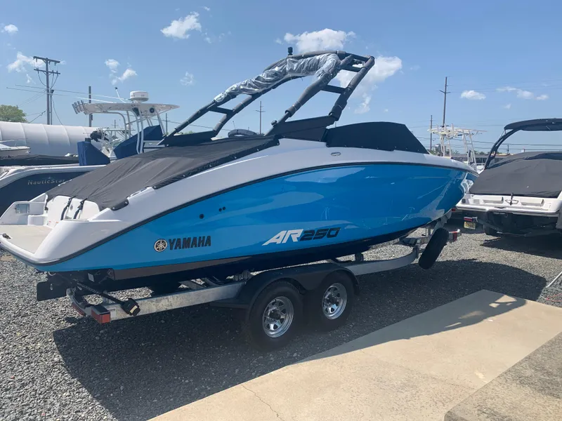 The Image of 2023 Yamaha Boats AR250, blue and white, on a trailer in a marina. - 0