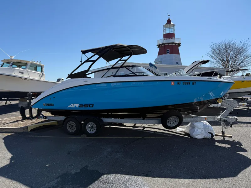 Slide: The Image of 2023 Yamaha Boats AR250 on trailer, blue hull, near lighthouse, sunny day. - 2
