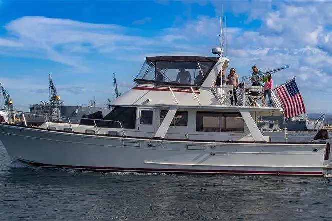 The Image of 1988 Offshore Yachts 48 Sedan cruising with passengers, American flag displayed, under clear blue skies. - 0