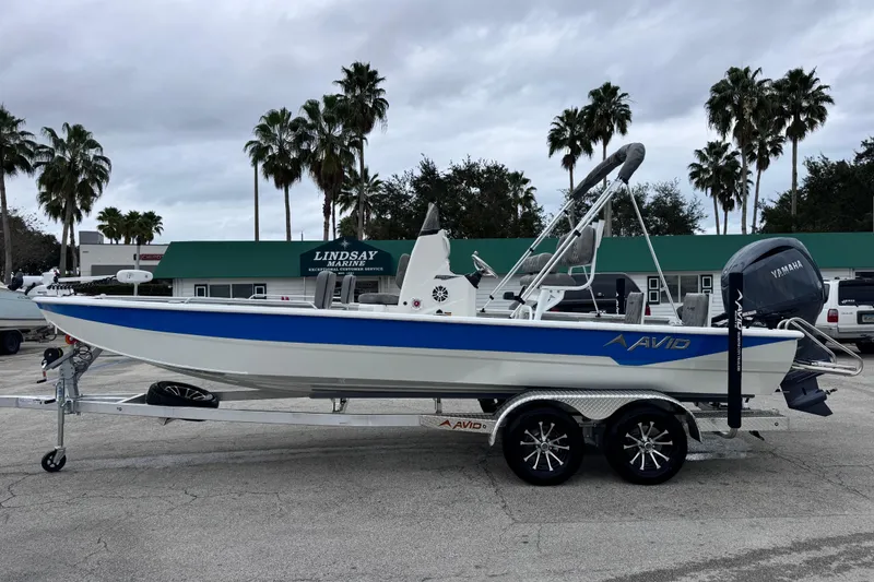 Slide: The Image of 2026 Avid 23 Fusion boat on trailer, parked at marina with palm trees. - 2