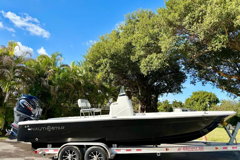 Slide: The Image of 2025 NauticStar 224 Bay boat on trailer, surrounded by lush greenery and blue sky. - 2