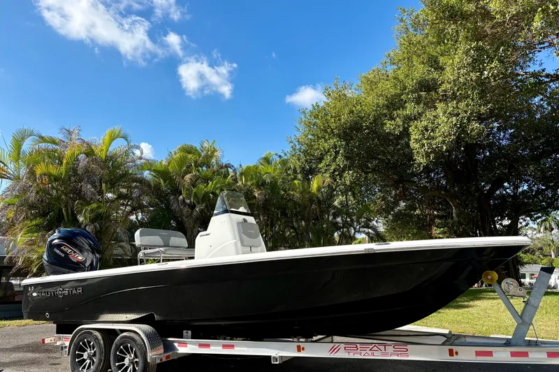 Slide: The Image of 2025 NauticStar 224 Bay boat on trailer, surrounded by lush greenery and blue sky. - 3