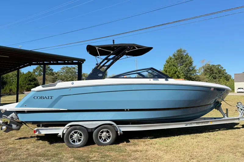 The Image of 2025 Cobalt R8 boat on trailer, blue hull, parked outdoors under clear sky. - 0