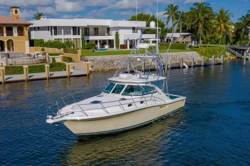Slide: The Image of 2004 Pursuit 3800 Express yacht cruising near waterfront homes, under a clear blue sky. - 2