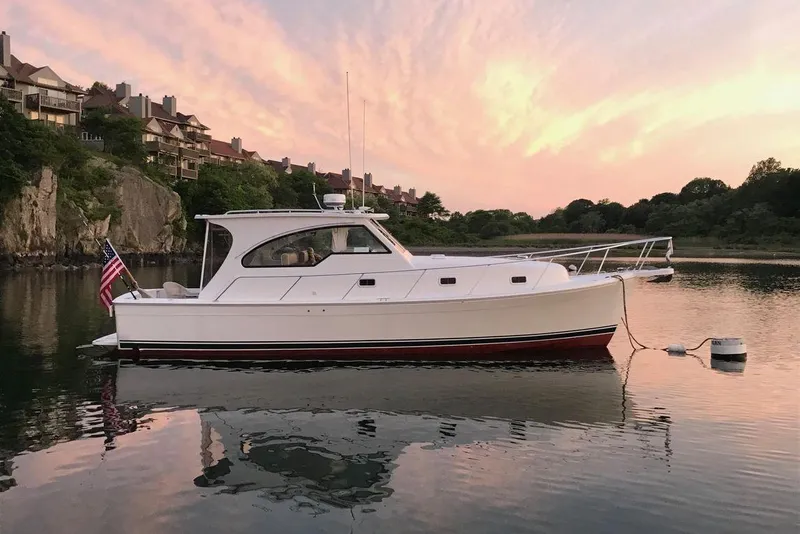 The Image of 2000 Mainship Pilot 34 Sedan boat on calm water at sunset, with scenic background. - 0