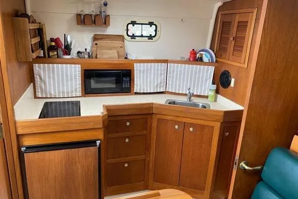 Slide: The Image of 2000 Mainship Pilot 34 Sedan kitchen with wood cabinetry, microwave, and compact sink. - 14