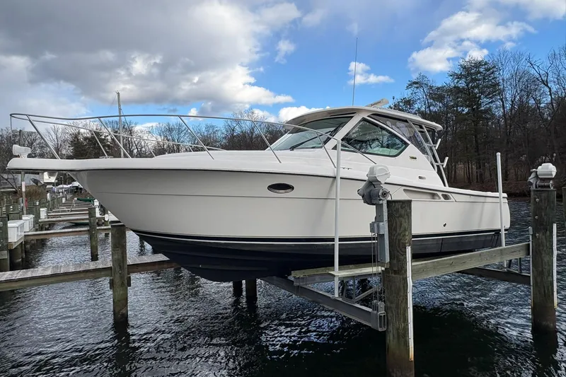 Slide: The Image of 2008 Tiara Yachts 3000 Open on lift, docked by wooded shoreline under cloudy sky. - 8