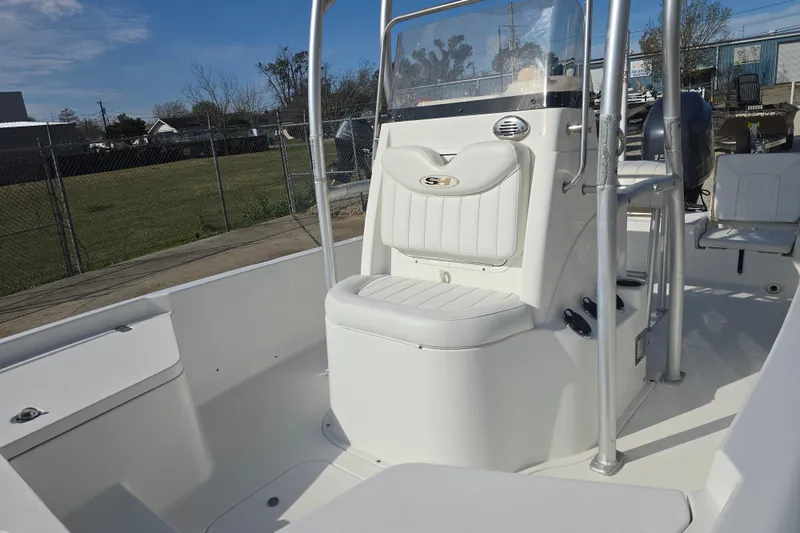 Slide: The Image of 2013 Sea Hunt XP 21 boat interior with white seating and console, docked outdoors. - 12
