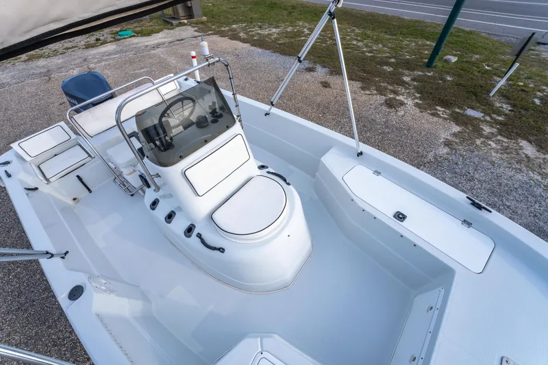 Slide: The Image of 2002 ProMaster 190 BAY boat interior with seating and steering console, parked on gravel. - 28