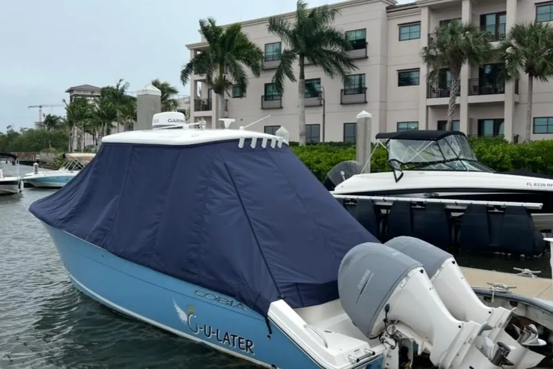 Slide: The Image of 2020 Cobia 262 Center Console boat docked with cover, near waterfront buildings. - 6