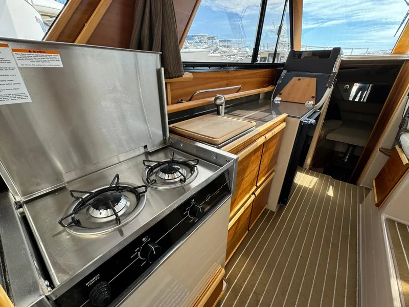 Slide: The Image of 2015 Cutwater C-26 boat interior with stove, wooden cabinetry, and striped flooring. - 12