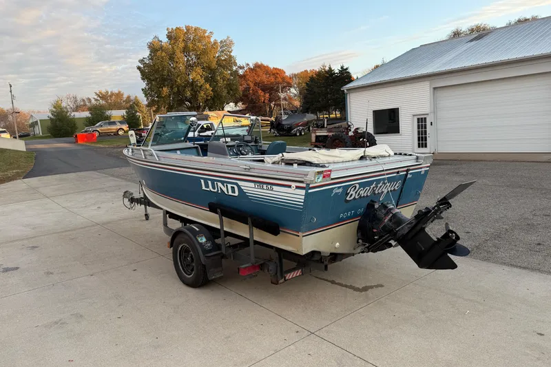 Slide: The Image of 1988 Lund boat on trailer, parked outside a garage, with autumn trees in the background. - 5