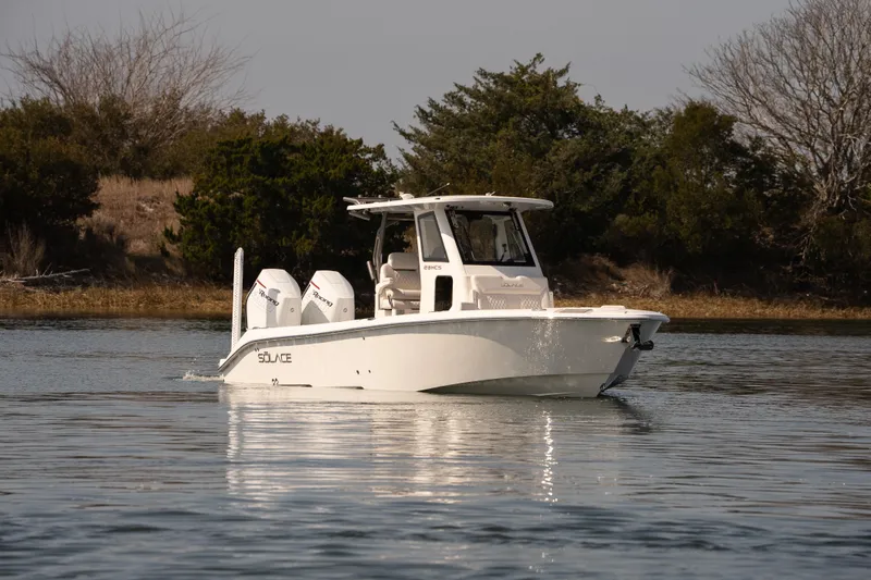 Slide: The Image of 2026 Solace 28 HCS boat cruising on calm water near a wooded shoreline. - 36