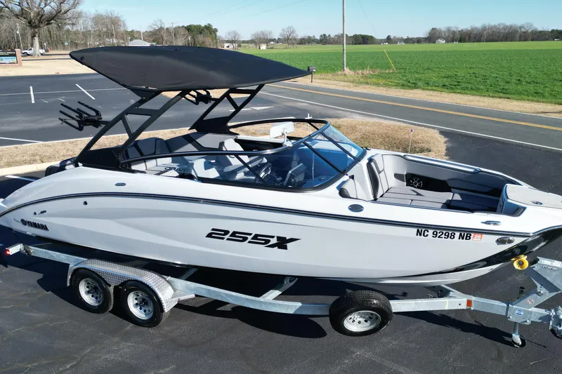 Slide: The Image of 2024 Yamaha Boats 255XE on trailer, parked outdoors, with black canopy and sleek design. - 18