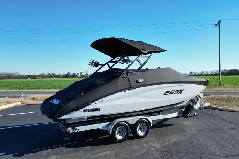 Slide: The Image of 2024 Yamaha Boats 255XE on trailer, covered, parked on asphalt near green field. - 25