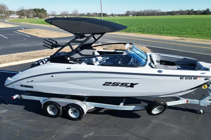 Slide: The Image of 2024 Yamaha Boats 255XE on trailer, parked near a road and green field. - 19