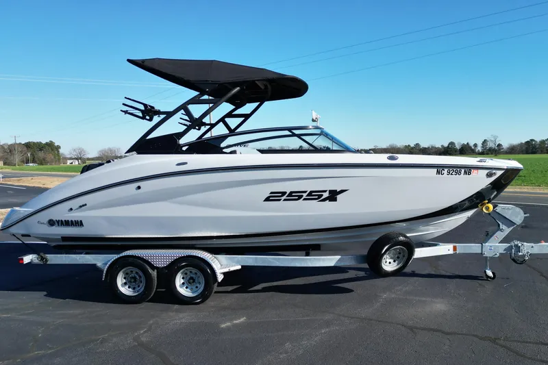 Slide: The Image of 2024 Yamaha Boats 255XE on trailer, sleek design, black canopy, parked outdoors. - 2