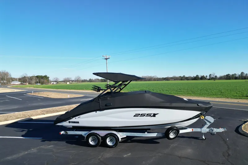Slide: The Image of 2024 Yamaha Boats 255XE on trailer, parked in open area under clear blue sky. - 22