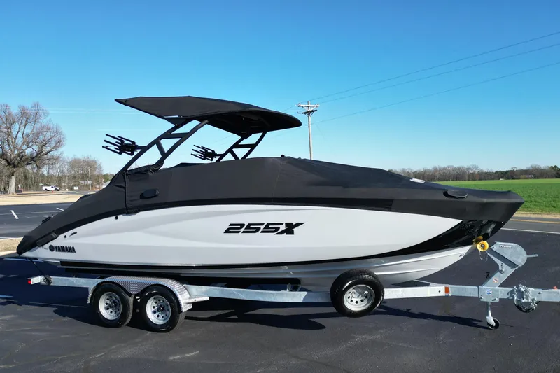 Slide: The Image of 2024 Yamaha Boats 255XE on trailer, covered, parked outdoors under clear blue sky. - 24