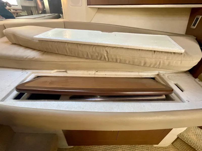 Slide: The Image of 2014 Sea Ray 330 Sundancer interior storage compartment with beige cushions and wooden panel. - 10
