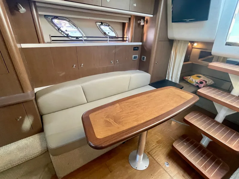 Slide: The Image of 2014 Sea Ray 330 Sundancer interior with wooden table, beige seating, and modern cabinetry. - 14