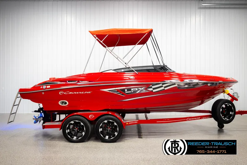 Slide: The Image of 2022 Crownline 220 LPX boat with red exterior and canopy, displayed indoors on a trailer. - 5