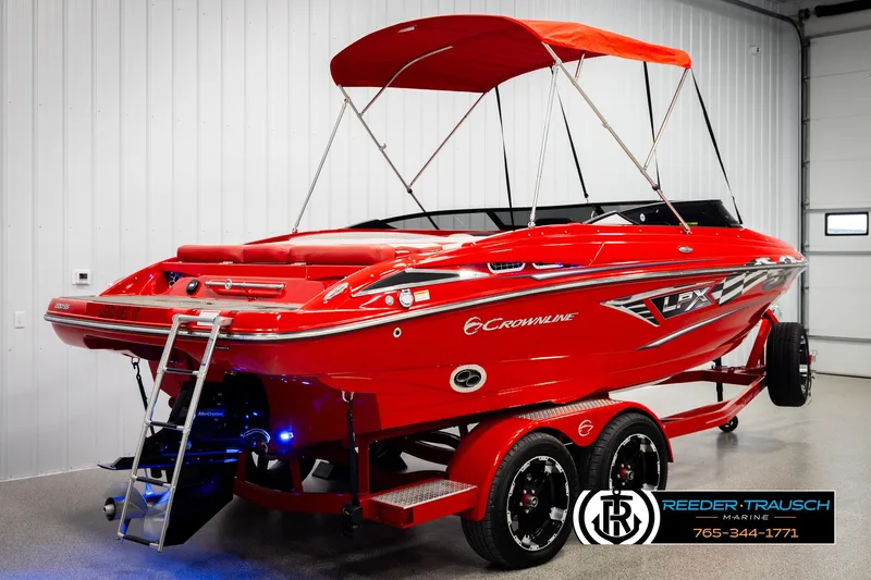 Slide: The Image of 2022 Crownline 220 LPX boat with red exterior and canopy, displayed indoors on a trailer. - 6