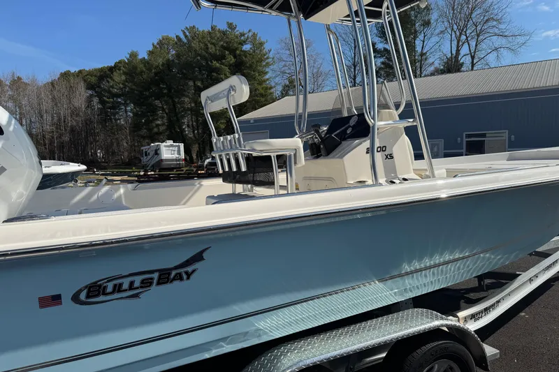 Slide: The Image of 2026 Bulls Bay 2200 boat on trailer, side view with trees and building background. - 9