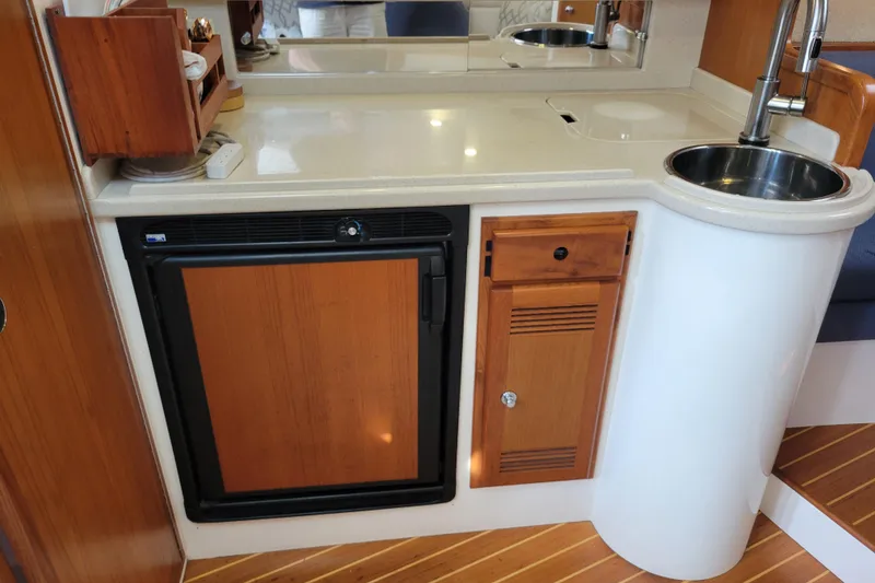 Slide: The Image of 1998 Cabo 31 Express boat interior with kitchenette, featuring sink, fridge, and wooden cabinetry. - 11