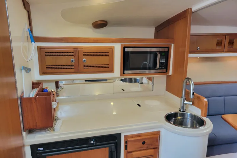 Slide: The Image of 1998 Cabo 31 Express boat interior with kitchenette, microwave, sink, and wooden cabinetry. - 12