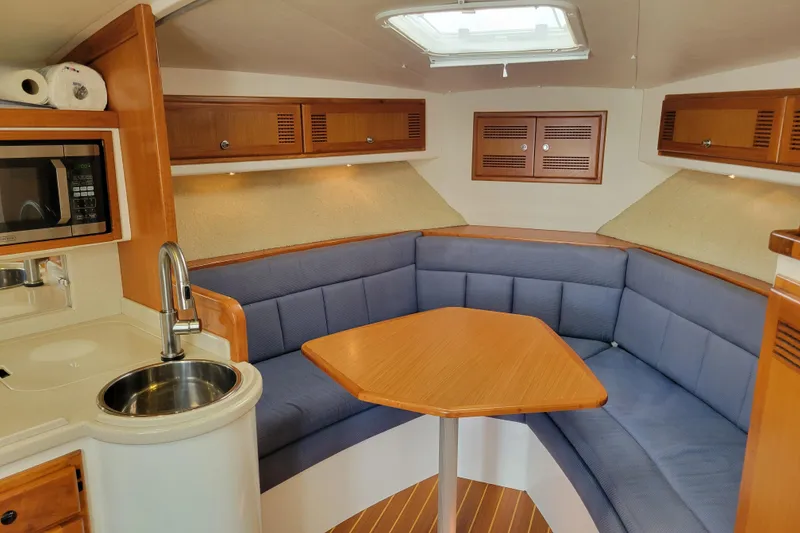Slide: The Image of 1998 Cabo 31 Express cabin interior with blue seating, wooden table, and kitchenette. - 8