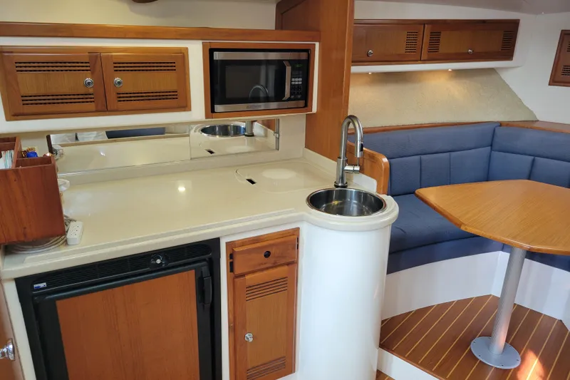 Slide: The Image of 1998 Cabo 31 Express interior with kitchenette, microwave, sink, and cozy seating area. - 9