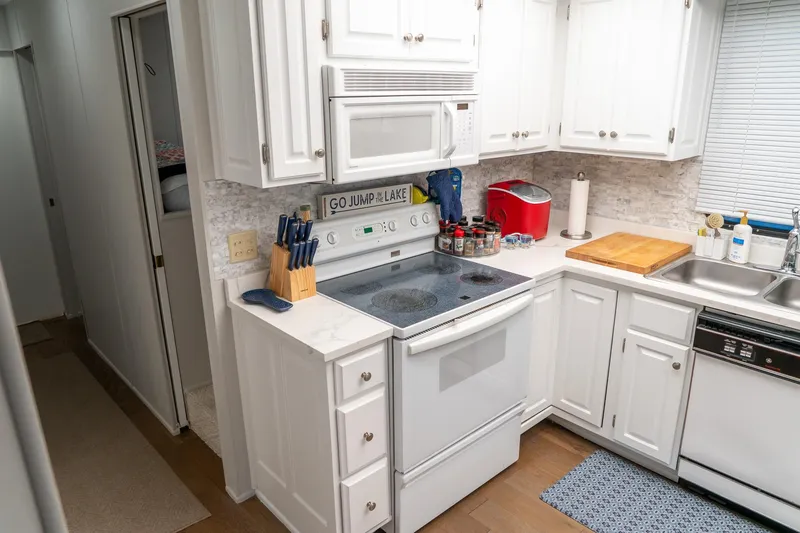 Slide: The Image of Compact kitchen in a 1996 Lakeview 66 x 16 Widebody Houseboat, featuring white cabinets and appliances. - 42