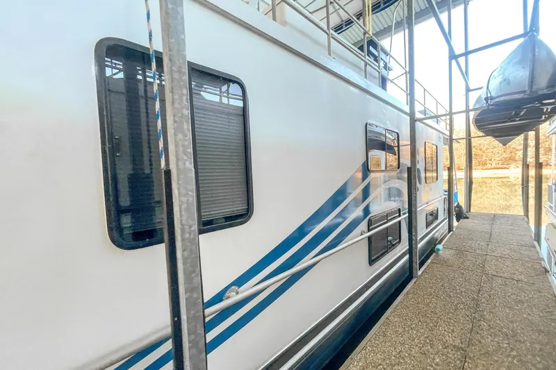 Slide: The Image of 1996 Lakeview 66 x 16 Widebody Houseboat docked, featuring blue stripes and multiple windows. - 6